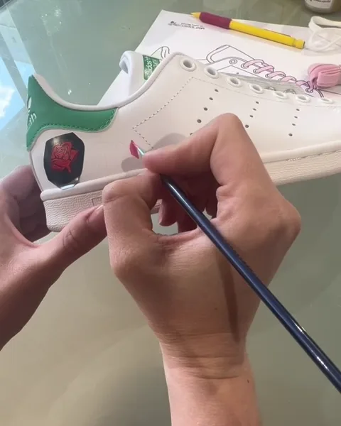 Une participante peint une rose sur sa Stan Smith pendant l'atelier