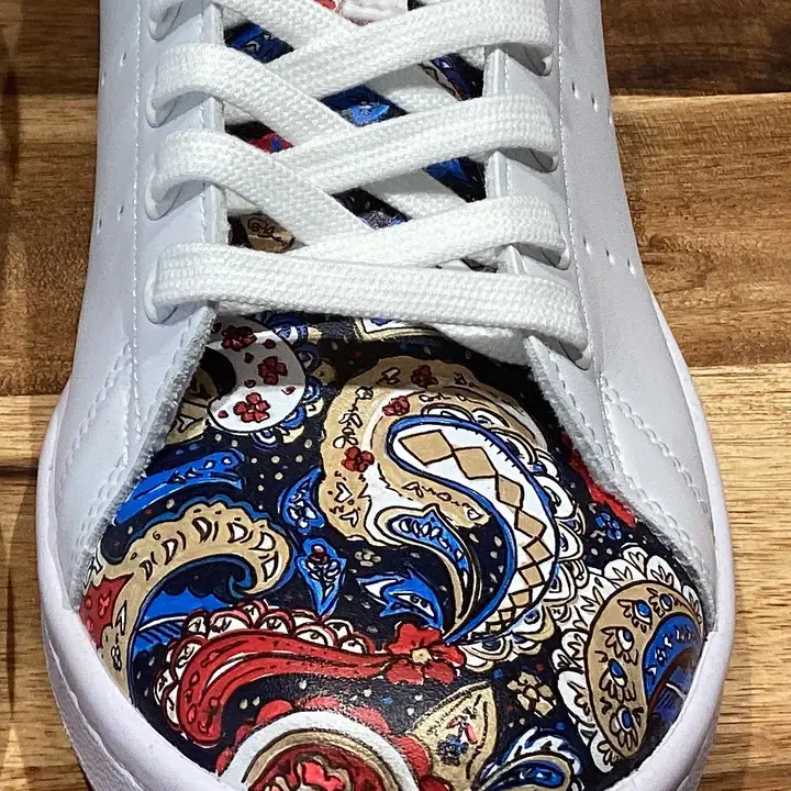 Gros plan d'une pointe de sneaker peinte à la main d'un motif paisley bleu, rouge et or